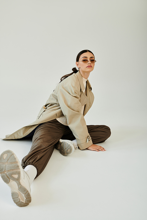 A fashionable young woman showcases her autumn style, sitting thoughtfully in a chic studio environment.