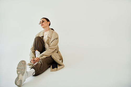 A young woman in a chic autumn outfit poses gracefully against a clean studio backdrop, embodying seasonal style.