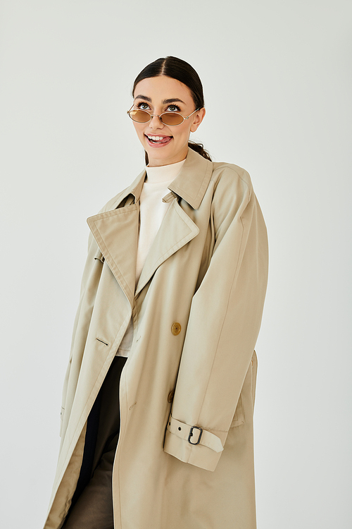 A young woman showcases her autumn style, wearing a trendy trench coat and smiling confidently in a studio.