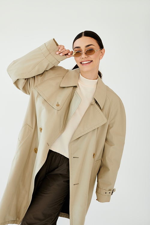 A young woman showcases a chic autumn look with confidence in a minimalist studio, exuding warmth and style.