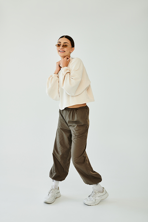 A cheerful young woman showcases her stylish autumn outfit while posing confidently in a bright studio environment.