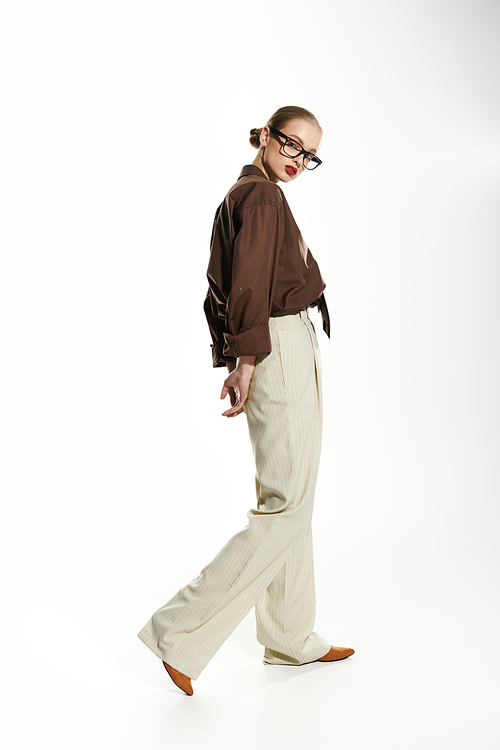 A stylish young woman walks confidently in a brown shirt and cream pants.