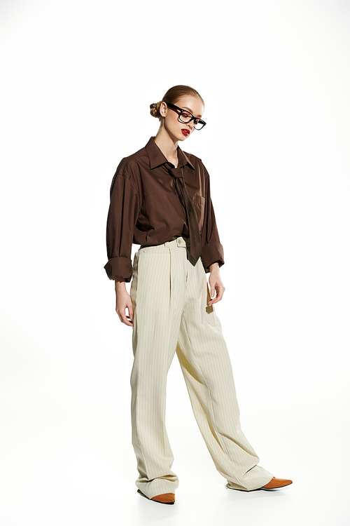 A young woman in a brown shirt and cream pants stands against a white background.