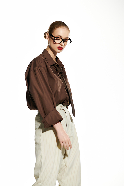 A young woman in a stylish brown shirt and white trousers looks down thoughtfully.