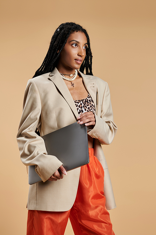 A young woman exudes confidence in trendy attire while holding a laptop, poised for adventure.