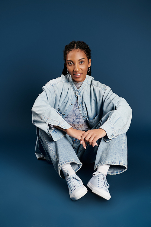 A young woman models her trendy denim outfit against a vibrant blue background.