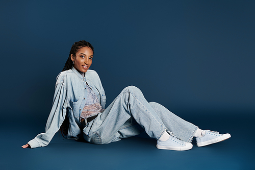 The confident young woman shines in her chic denim outfit against a solid backdrop.