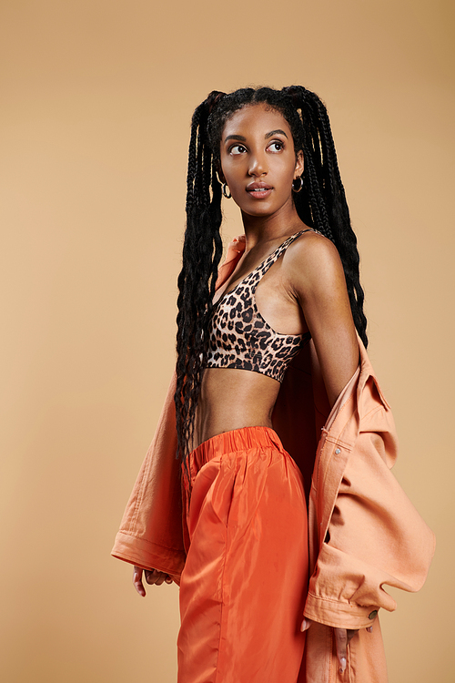 Dressed in chic attire, a young woman exudes flair while posing against a warm backdrop.