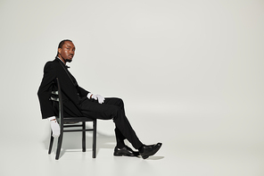 A young African American man elegantly dressed in a suit and vest sits confidently on a chair, showcasing style.