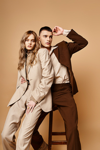 appealing young woman in pastel suit looking at camera next to her handsome boyfriend on chair