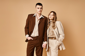 debonair young woman in stylish suit posing with her handsome boyfriend and looking at camera