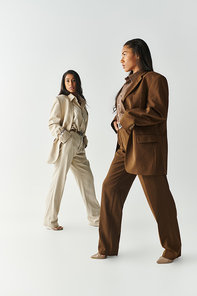 Two young women exhibit trendy fashion choices in a minimalist studio, radiating confidence.