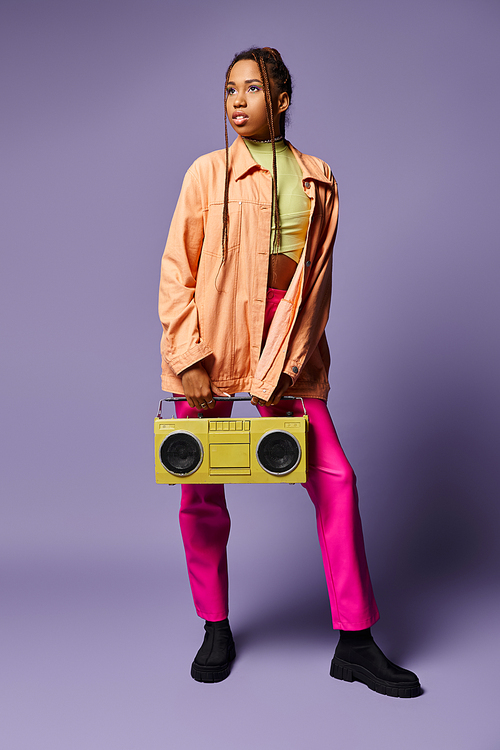 dreamy african american girl with dreadlocks standing with retro boombox on purple backdrop