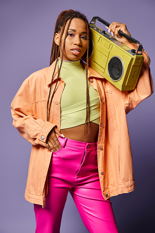 stylish african american girl with dreadlocks standing with retro boombox on purple backdrop