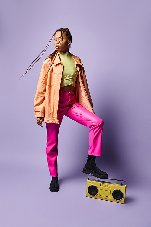 stylish african american girl with dreadlocks stepping on retro boombox on purple backdrop