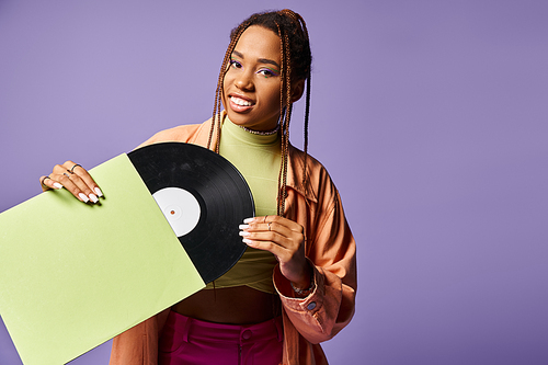 happy young african american woman in her 20s with dreadlocks holding vinyl disc on purple backdrop