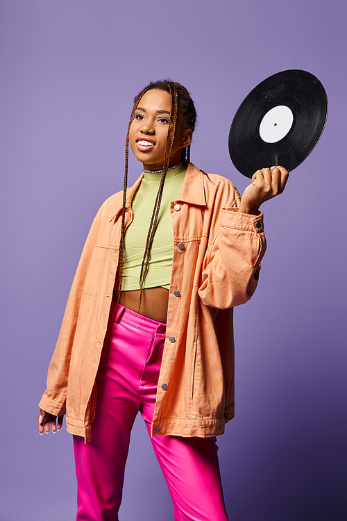 happy young african american girl in her 20s with dreadlocks holding vinyl disc on purple backdrop