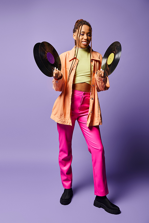 happy african american girl in her 20s with dreadlocks comparing vinyl discs on purple backdrop