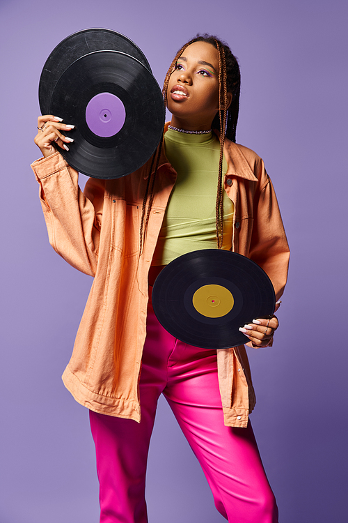 pensive african american girl in her 20s with dreadlocks holding vinyl discs on purple backdrop