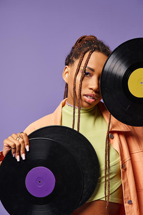 young african american girl in her 20s with dreadlocks posing with vinyl discs on purple backdrop