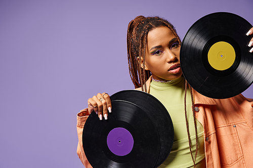 young african american woman in her 20s with dreadlocks posing with vinyl discs on purple backdrop