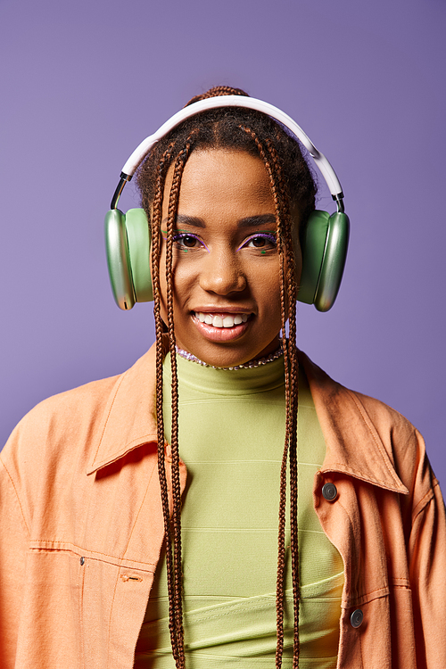 jolly african american woman in vibrant attire with wireless headphones on purple backdrop