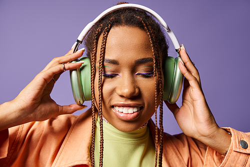 pretty african american woman in vibrant attire with wireless headphones on purple backdrop