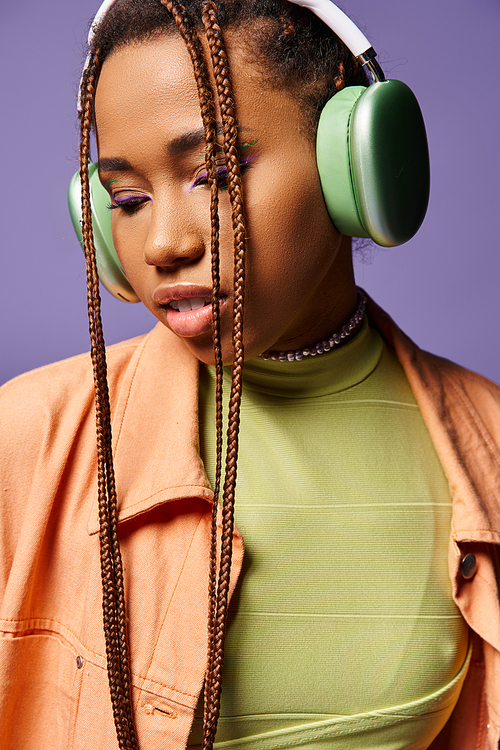 pretty african american girl in 20s listening music in wireless headphones on purple backdrop