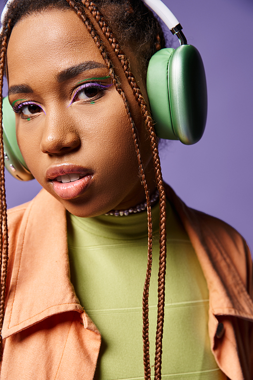 serene african american girl in 20s listening music in wireless headphones on purple backdrop