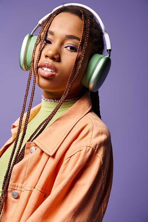 pretty african american girl in 20s listening music in wireless headphones on purple background