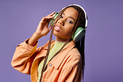 pretty african american woman in 20s listening music in wireless headphones on purple background