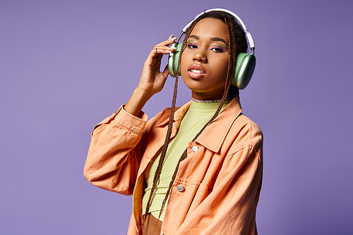 alluring african american woman in 20s listening music in wireless headphones on purple background