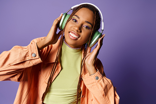 pleased african american girl in 20s listening music in wireless headphones and looking at camera