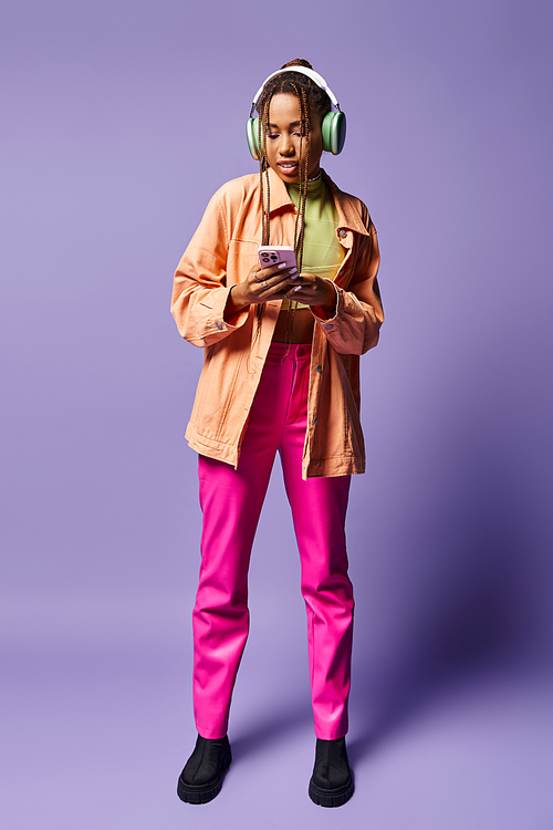 happy african american woman in her wireless headphones using smartphone on lilac backdrop