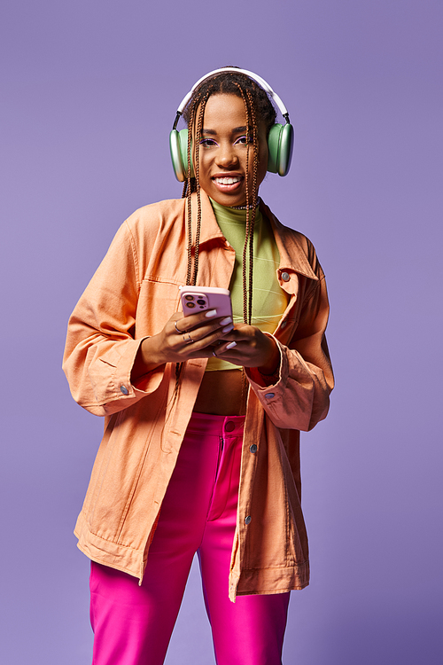 happy african american woman in green wireless headphones using smartphone on lilac backdrop