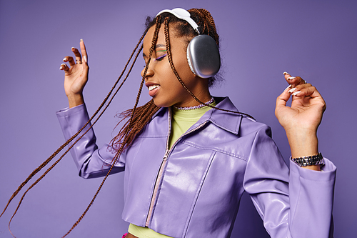 happy young african american woman with wireless headphones enjoying music on purple background