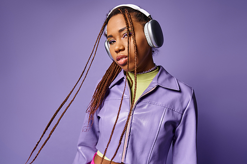 young african american woman with dreadlocks and wireless headphones enjoying music on purple