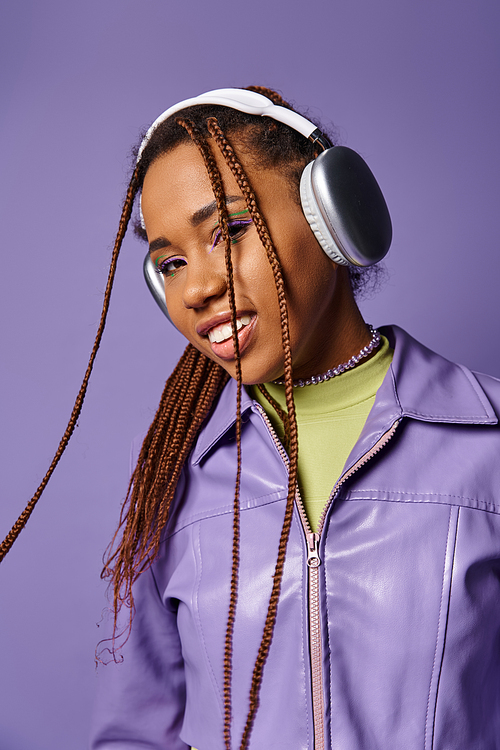 Smiling young african american woman with wireless headphones enjoying music on purple background