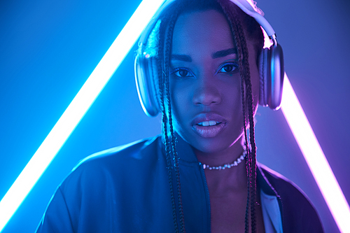 portrait of african american girl in dreadlocks and headphones in studio with blue fluorescent light