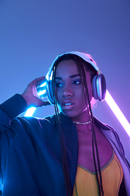 stylish african american girl in dreadlocks and headphones in studio with blue fluorescent light