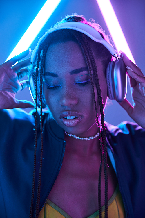 young african american girl in dreadlocks and headphones in studio with blue fluorescent light