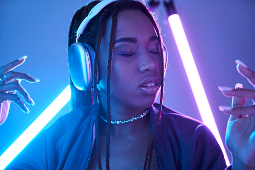 young african american girl in headphones enjoying music in studio with blue fluorescent light