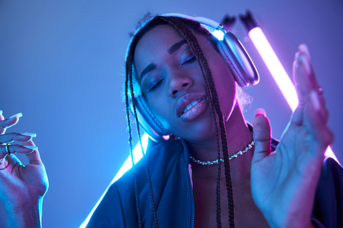 young african american woman in headphones enjoying music in studio with blue fluorescent light