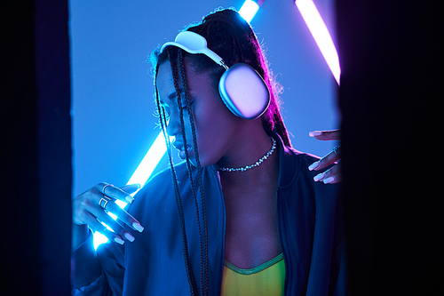 pretty african american woman in headphones enjoying music in studio with blue fluorescent light