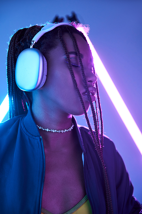 pretty african american woman in headphones enjoying music in studio with fluorescent light