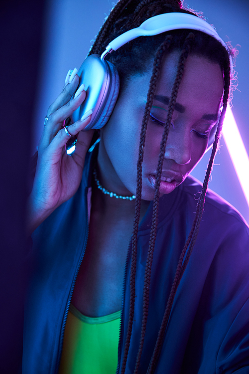 pretty african american girl in headphones enjoying music in studio with fluorescent light