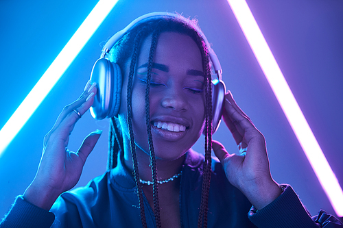 cheerful african american woman in headphones enjoying music in studio with fluorescent light