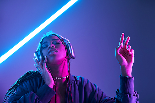 ecstatic african american woman in headphones enjoying music in studio with fluorescent light