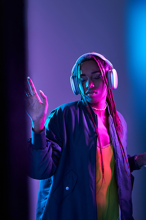 african american girl in wireless headphones enjoying music in studio with neon light, dance