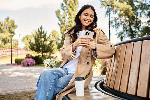 She relaxes on a bench, dressed warmly for autumn, with a coffee cup by her side.